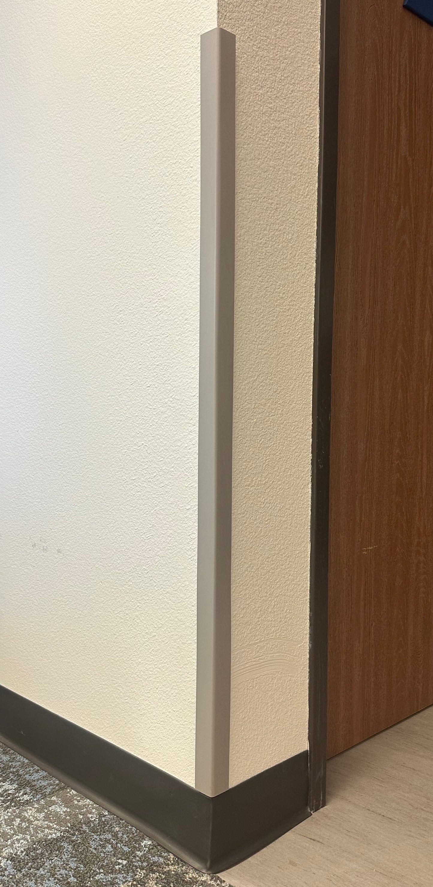 A close-up of a Flexitions grey/beige protective wall corner guard installed on the corner of a room.