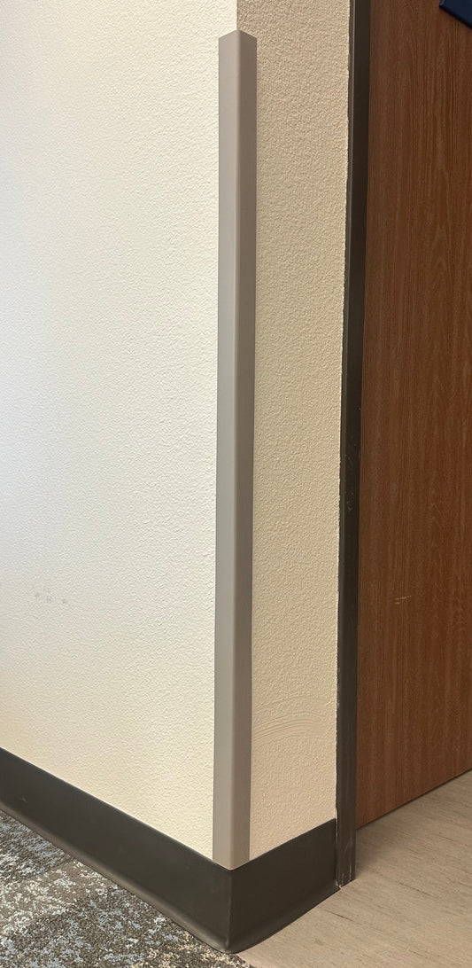 A close-up of a Flexitions grey/beige protective wall corner guard installed on the corner of a room.